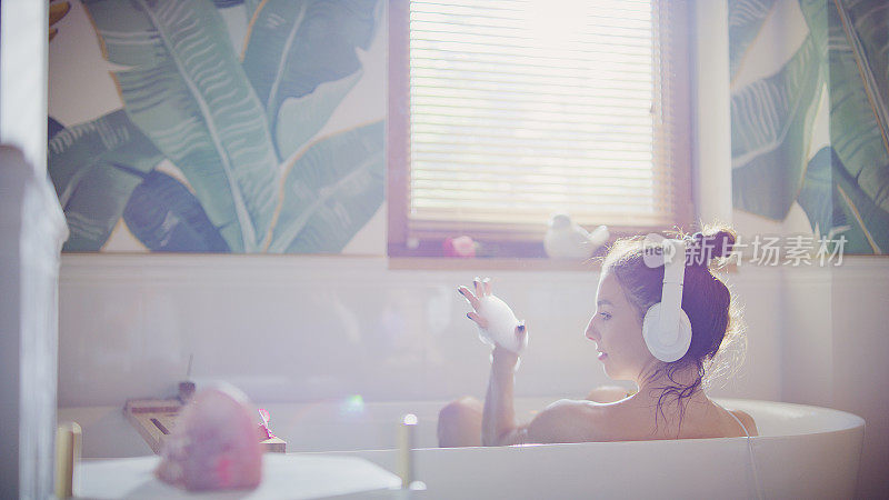 美丽的女人在现代浴室放松。听音乐。对着想象中的麦克风表演