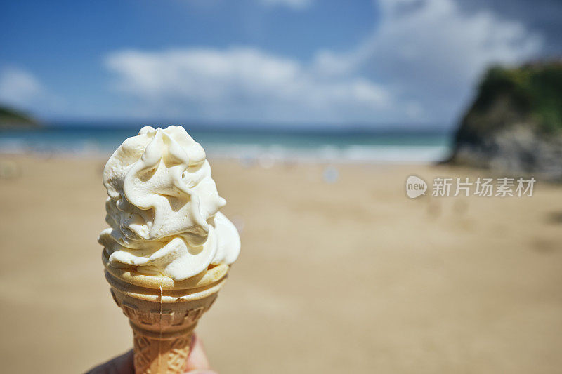 6月一个阳光明媚的日子，在康沃尔郡纽基的托万海滩，一只手拿着冰淇淋蛋筒。