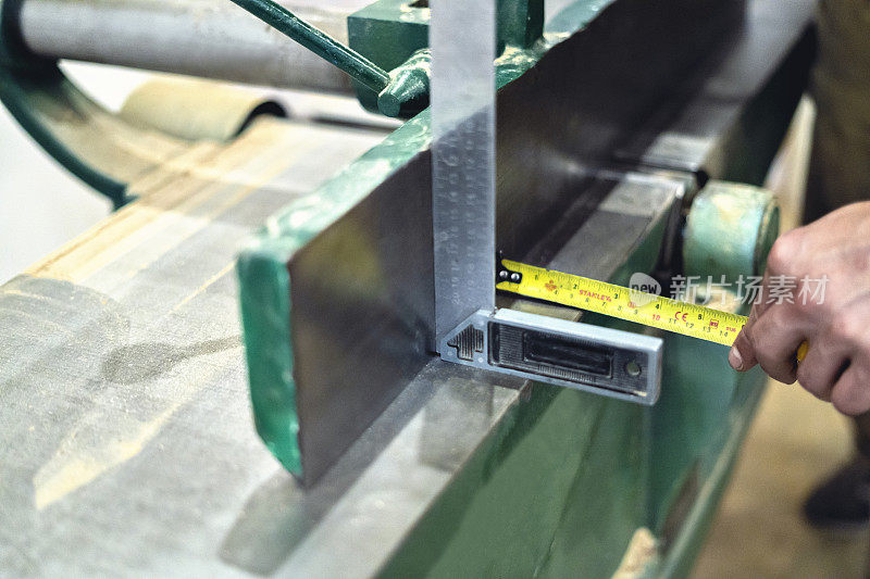木匠用米和尺测量木工车间使用的机器。