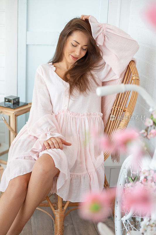 年轻美丽的女人的肖像长发穿着粉红色的夏季连衣裙，坐在柳条椅附近的白色自行车。