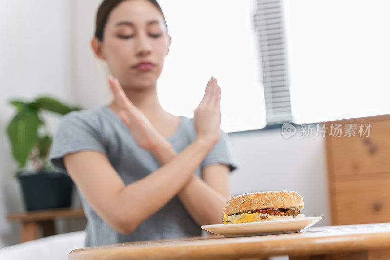年轻女子做手势拒绝桌上的汉堡包