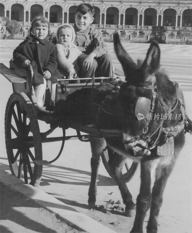 黑白照片拍摄于1960年，三个孩子在西班牙塞维利亚驴拉的马车上摆姿势