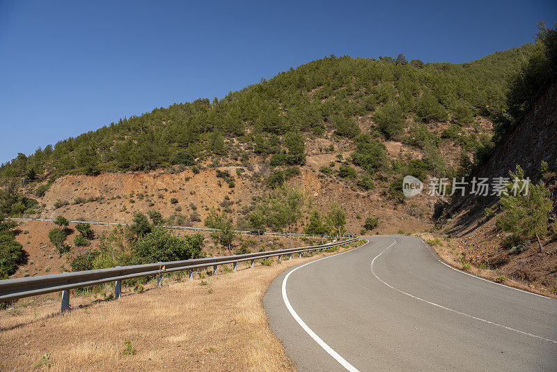 道路抱着蜿蜒的山坡，穿过陡峭的火山地形，在森林稀疏的山上，左侧有护栏