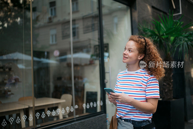 迷人的女人看着她所在城市的商店橱窗