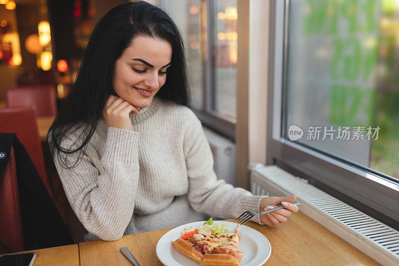 年轻漂亮的女人在餐厅吃披萨