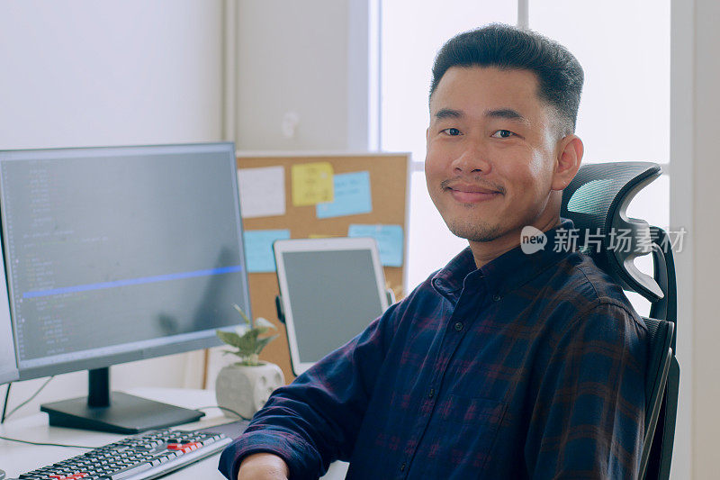 画像年轻的亚洲男人开发程序员，软件工程师，IT支持，看着相机和微笑享受在办公室工作。