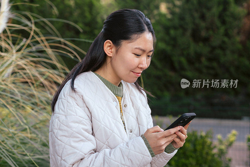 年轻的亚洲女子在外面用智能手机