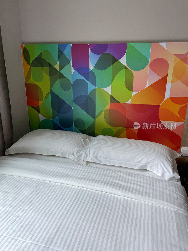 酒店双人床上的白色枕头和羽绒被床罩，图案，彩色床头板，红色，橙色，粉红色，绿色和蓝色材料床头，重点在前景
