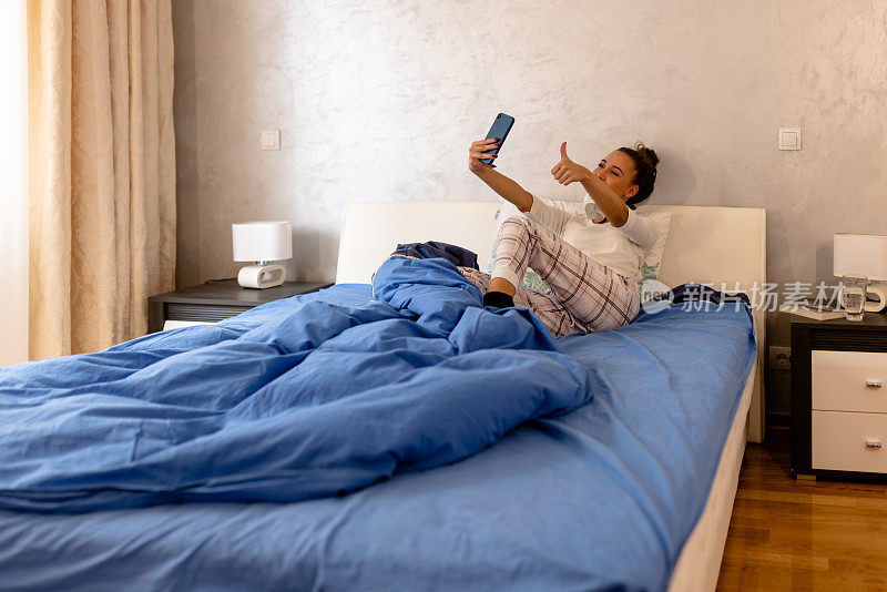 一张年轻美女躺在床上用智能手机视频通话的照片。