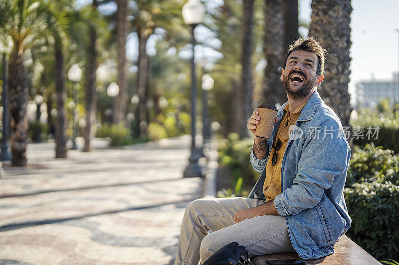 一个快乐的旅行者坐在城市街道上，喝着咖啡，休息一下。
