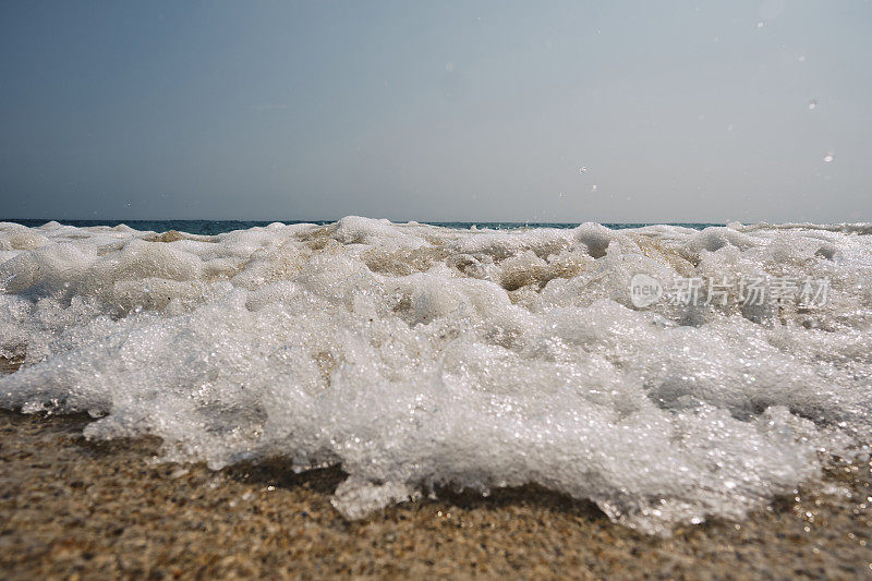 6月的一个晴朗的日子里，康沃尔郡佩顿温德海滩的海岸线上，一波海浪冲进相机的特写。