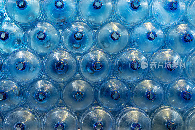 一加仑大小的塑料瓶整齐有序地摆放在矿泉水工厂内。瓶子等待灌装过程，代表生产的初始阶段。