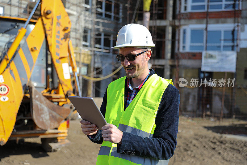 男建筑师在工地使用数码平板电脑，他穿着防护背心和头盔