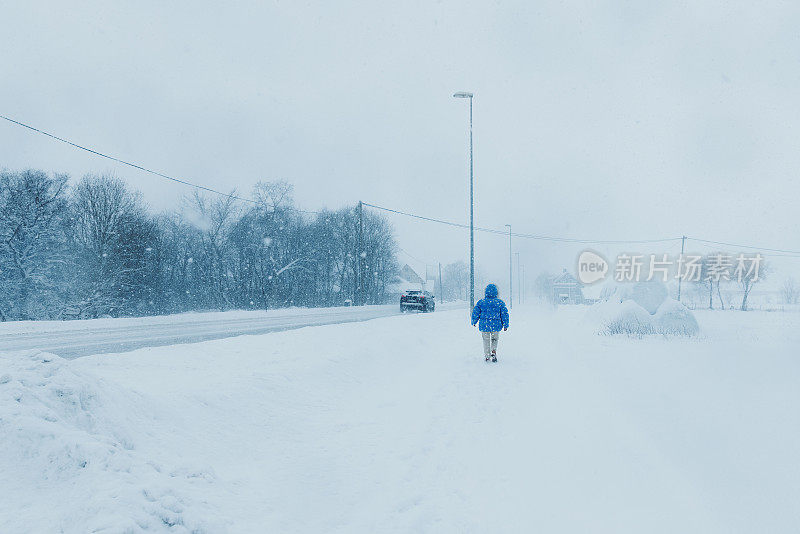 一名穿着蓝色外套的女子在大雪中漫步在斯堪的纳维亚村庄的街道上，欣赏冬天