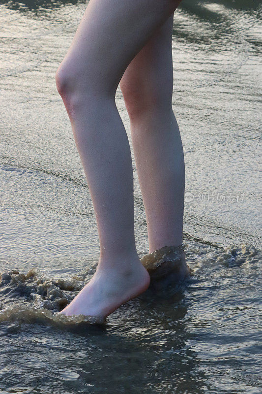 特写照片中，无法辨认的白人女子在水深及脚踝的海水中划桨，海浪，腿部和光脚，海边沙滩沙滩，重点放在前景