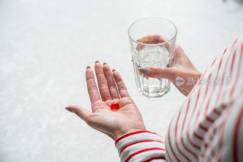 一个女人的手掌上放着红色药丸，手里拿着一杯水。一位妇女在家服药。