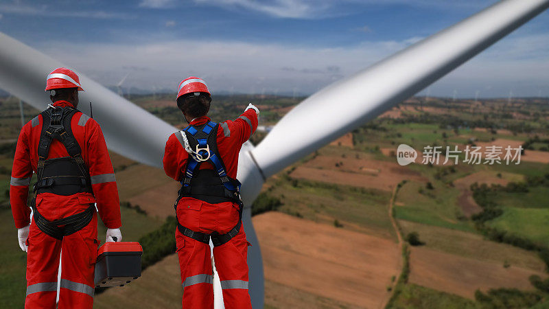 风力涡轮机农场，穿着红色安全制服的风力涡轮机技术人员和工程师在风车上工作