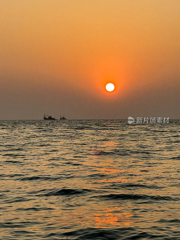 太阳在海上橙色的天空中落下，油轮在海上的地平线上，忧郁的灰色云岸，太阳在水中的反射