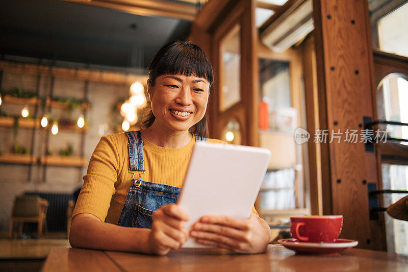 年轻的日本女子在咖啡馆喝咖啡，并在平板电脑上工作