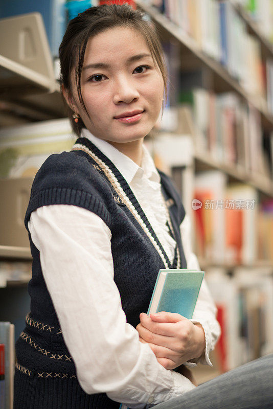 女孩在书架旁抱着一本书