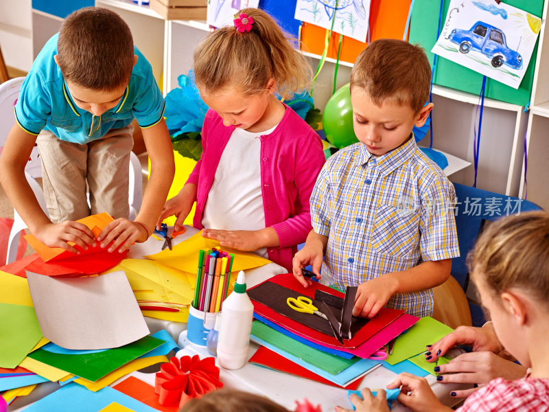 幼儿园桌上拿着彩纸的孩子们