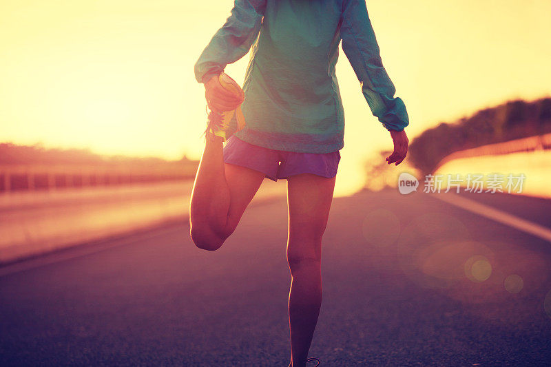 年轻的健身女性跑步伸展腿在城市道路上