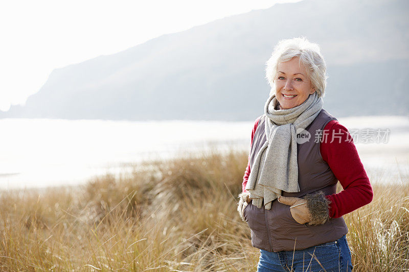 在冬天的海滩上穿过沙丘的资深妇女