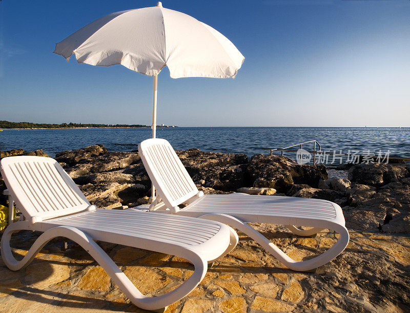 海边有两把躺椅和一把阳伞