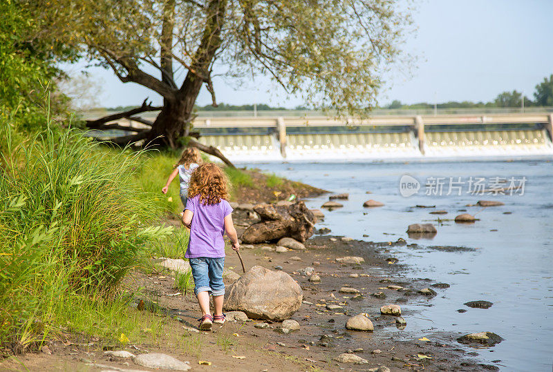 两个年轻女孩在大坝附近的河岸上行走