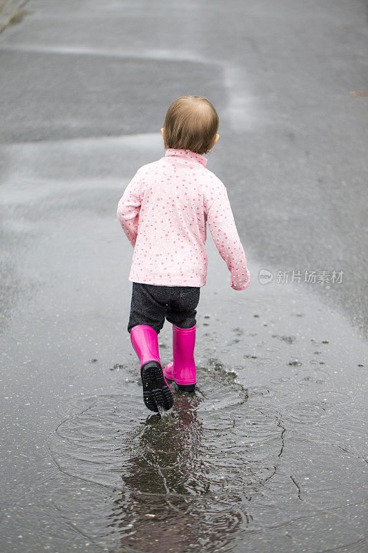 蹒跚学步的孩子穿着雨靴走过水坑