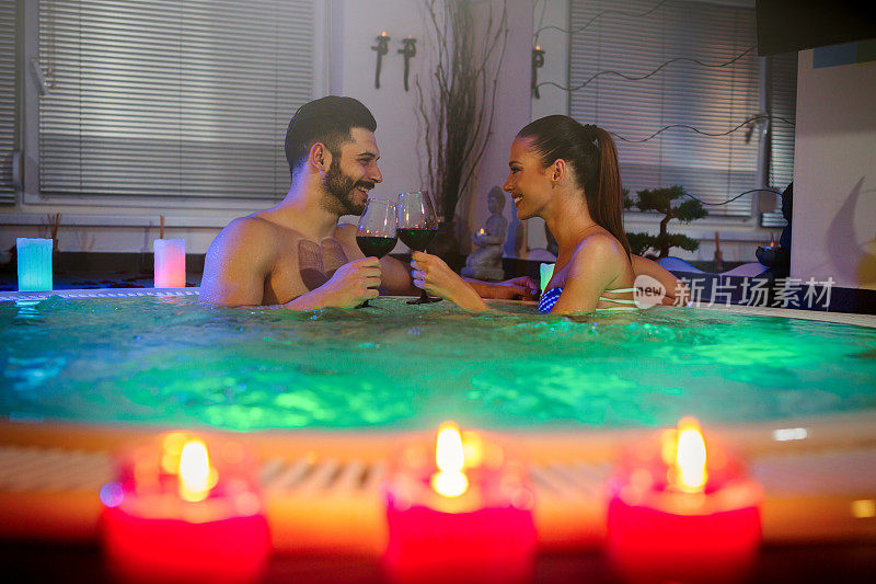 欢快的夫妇在冒泡的热水浴缸里喝红酒。