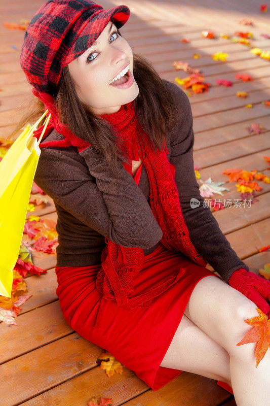 微笑的女人拿着购物袋坐在秋天的树叶上
