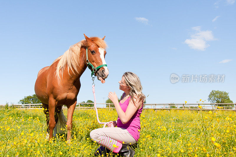 美丽的女孩和她有趣的小马在花丛中