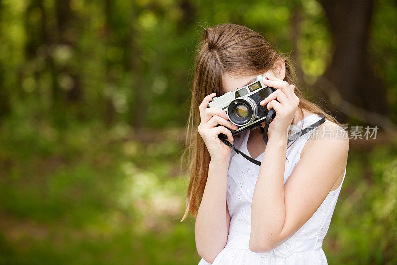 年轻女孩在户外用老式相机拍照