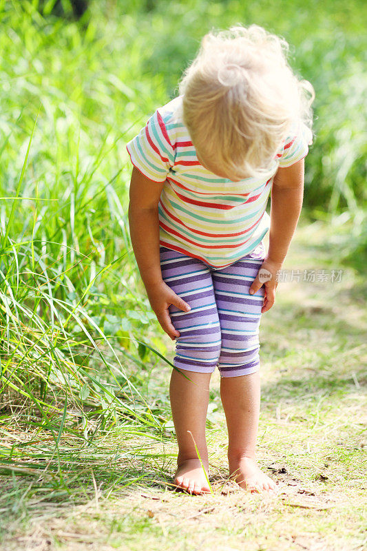 蹒跚学步的小女孩正在看草丛中的昆虫