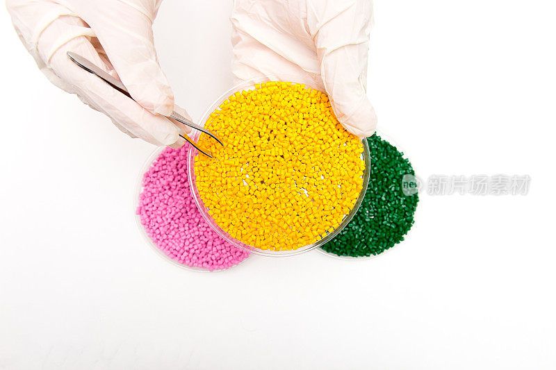 塑料颗粒。颗粒状聚合物的着色剂。手上拿着塑料小球，戴着手套和镊子