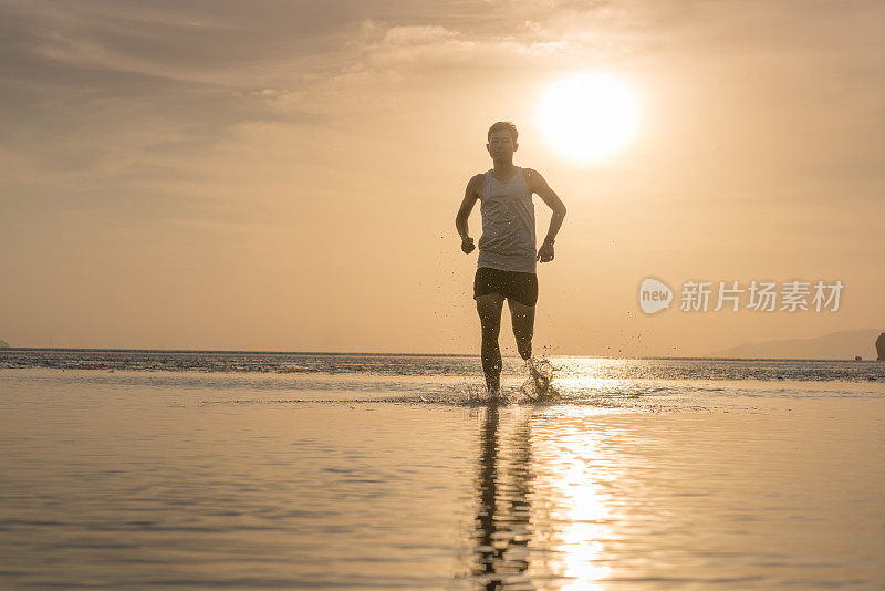 年轻的亚洲男子在海滩上奔跑，夕阳为背景