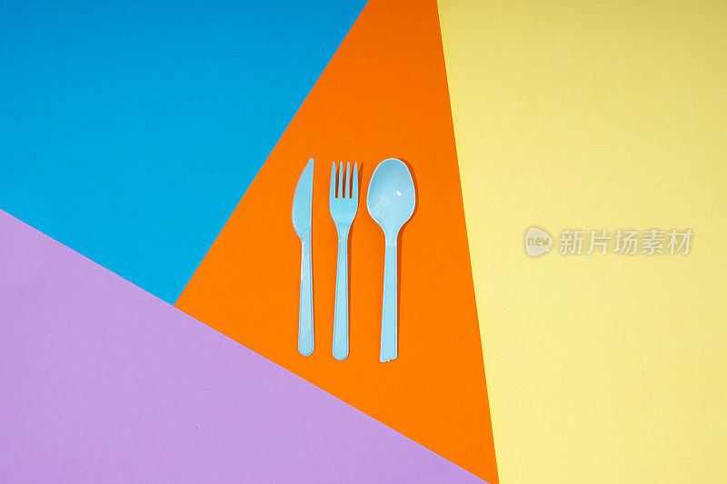勺子，刀，叉在橙色，黄色，紫色和蓝色的纸张背景