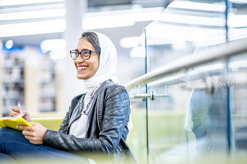 穆斯林学生微笑着在现代大学图书馆学习