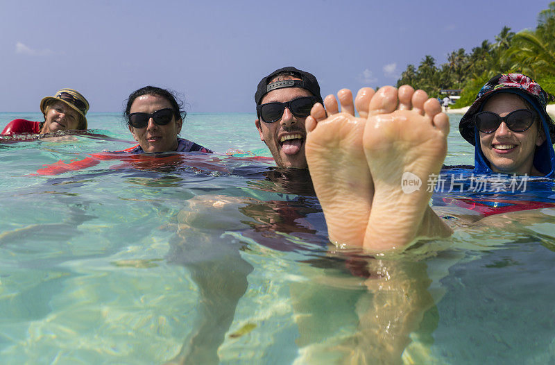 马尔代夫卡福环礁迪古拉岛的“比基尼海滩”上，一名女子翘着腿坐在浅水里，而一名男子正在露出舌头