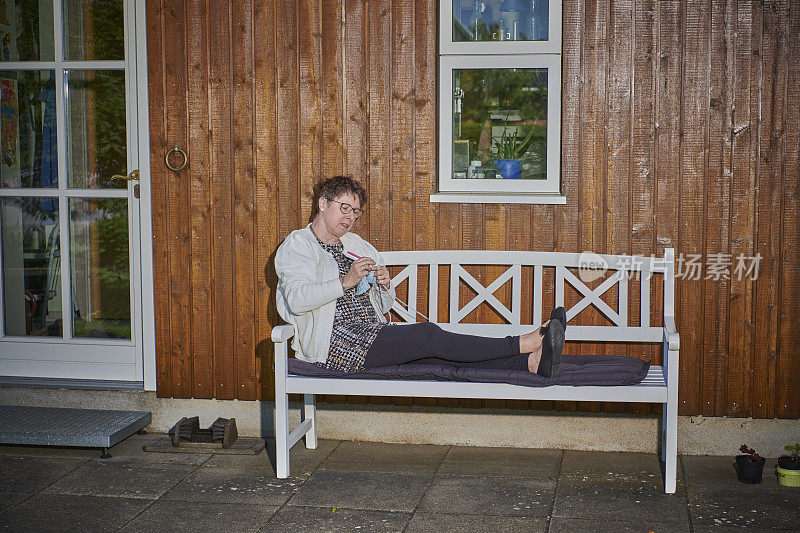 退休妇女享受时间在户外长凳上编织