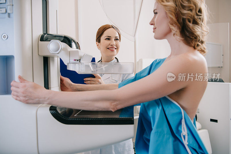 微笑的放射科医生站在病人旁边，在x光机上做乳房x光诊断