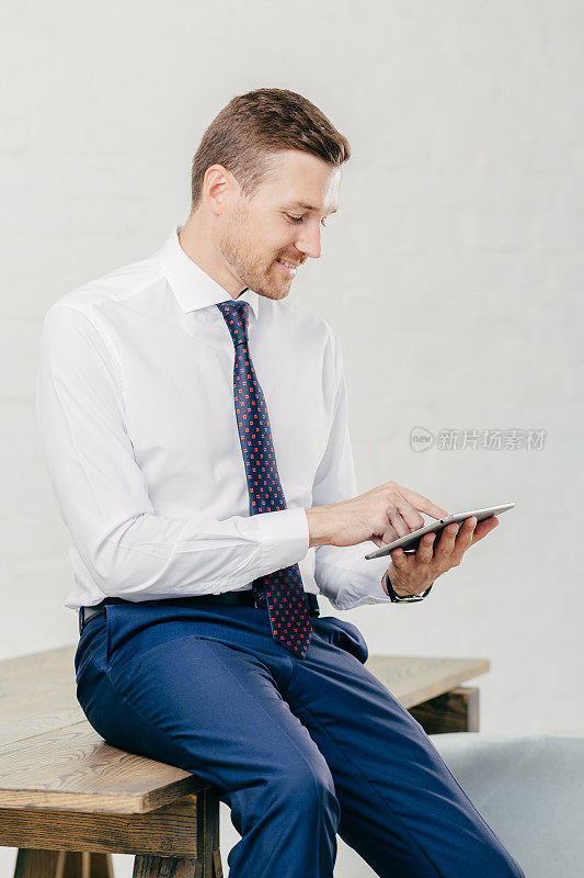 讨人喜欢的年轻商人在手提电脑上查看电子邮件，在互联网网页上观看视频，使用免费网络连接，穿着优雅的正式服装，在白色背景下与世隔绝
