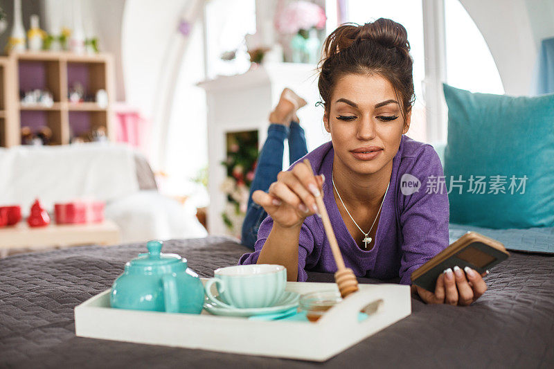 年轻女子一边放松一边用手机在茶里滴蜂蜜