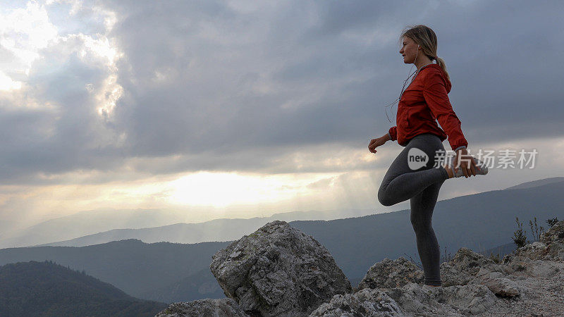 日出时，年轻的女性越野跑运动员在山脊上伸展身体