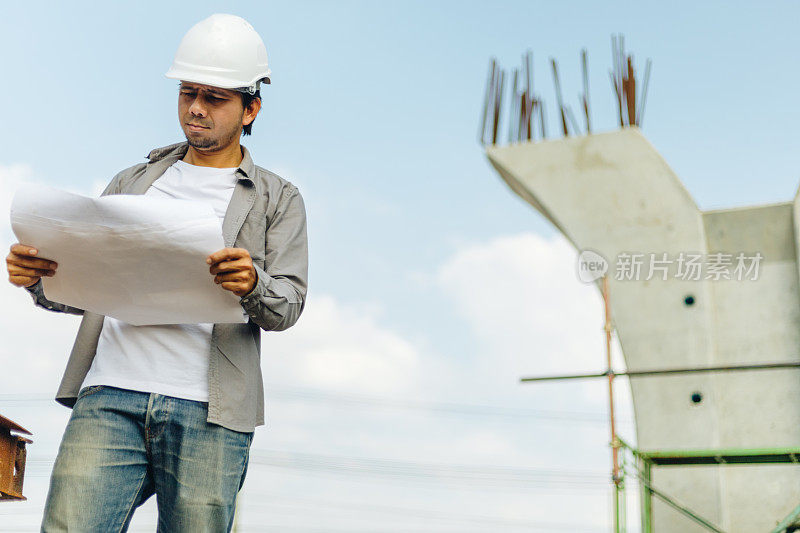亚洲工程师男子戴安全帽和检查蓝图在施工现场，工程师建筑师施工现场规划概念