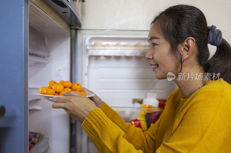 亚洲妇女从家庭厨房冰箱里拿橘子