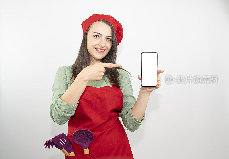 家庭主妇女厨师厨师或面包师在厨师的帽子孤立在白色的背景。女人拿着空白屏幕的手机宣传内容。模拟复制空间的概念