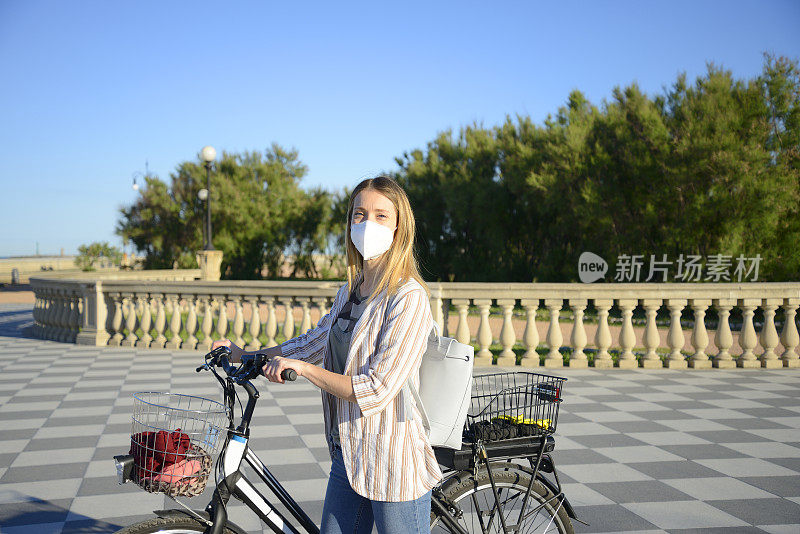 年轻女子戴着保护面罩骑着电动自行车在海边