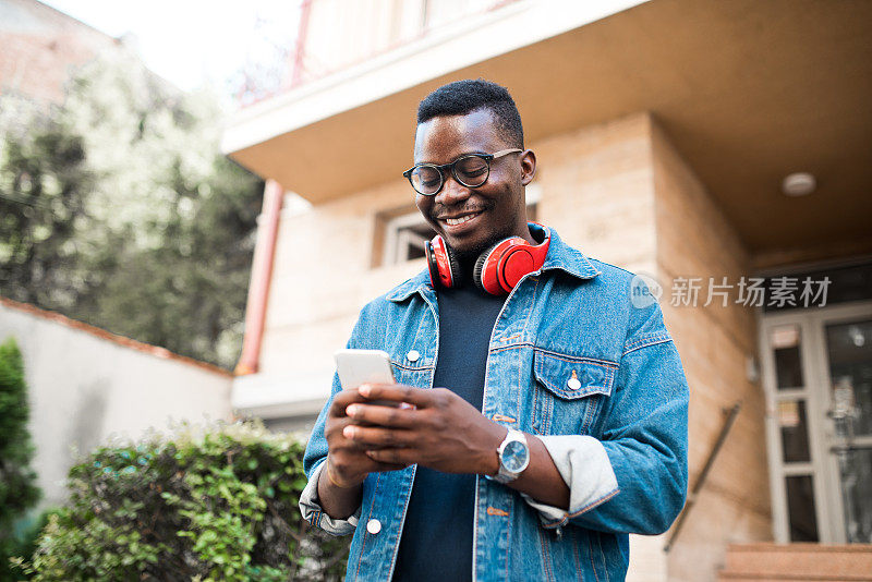 一个快乐的年轻非洲裔美国人走出家门，使用手机的肖像